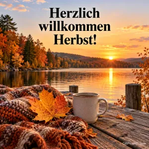 Ein Ahornblatt, eine Strickdecke und eine Tasse auf einem Steg am See bei Sonnenuntergang mit dem Text "Herzlich willkommen Herbst!".