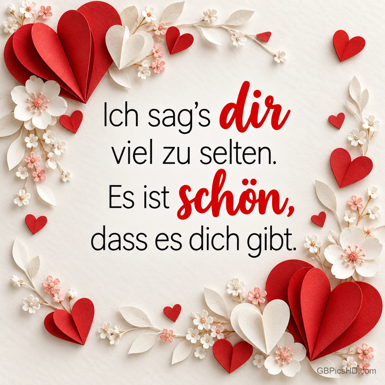 Ein Rahmen aus roten Papierherzen und kleinen Blüten umgibt den Spruch "Ich sag's dir viel zu selten. Es ist schön, dass es dich gibt."