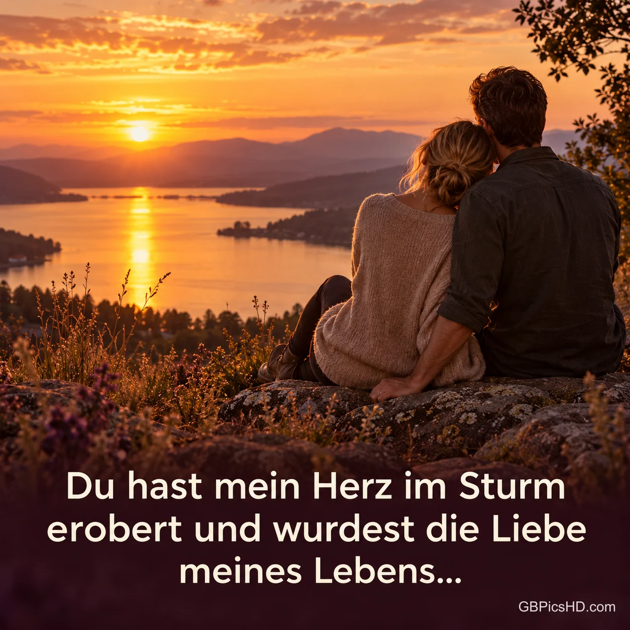 Ein Paar sitzt aneinandergekuschelt auf einem Felsen über einem See und schaut in den orangefarbenen Sonnenuntergang über den Bergen, darunter ein romantischer Spruch