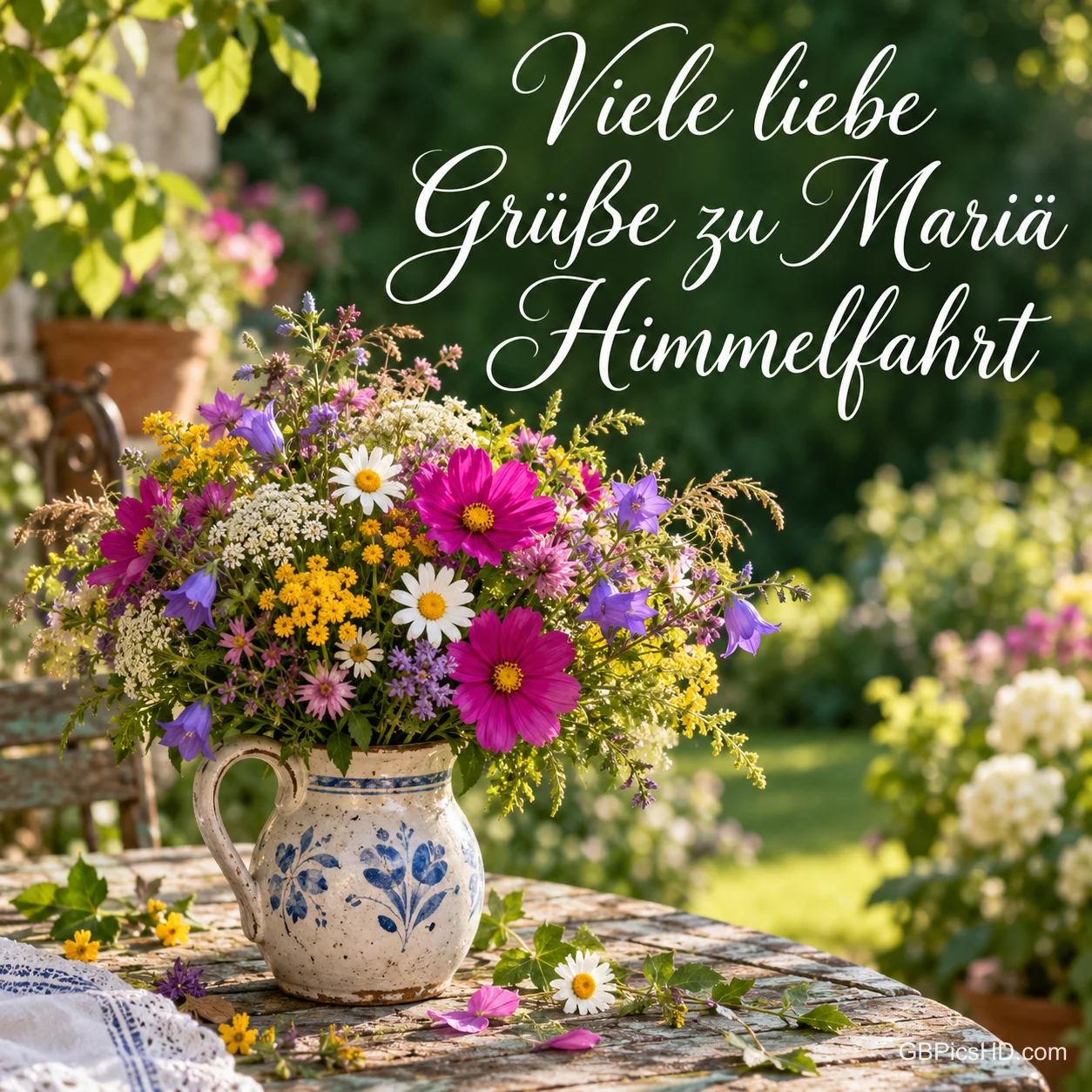 Ein bunter Wildblumenstrauß in einem Krug auf einem Gartentisch mit dem Gruß "Viele liebe Grüße zu Mariä Himmelfahrt". Ein bunter Wildblumenstrauß in einem Krug auf einem Gartentisch mit dem Gruß "Viele liebe Grüße zu Mariä Himmelfahrt".