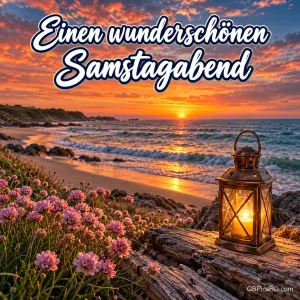 Leuchtende Laterne auf Treibholz zwischen rosa Strandnelken an einer felsigen Küste, die Sonne versinkt farbenprächtig im Meer, darüber ein Samstagabendgruß