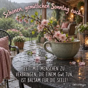 Blütenzweige in einer großen Tasse stehen auf einem regennassen Terrassentisch: "Schönen, gemütlichen Sonntag euch...".