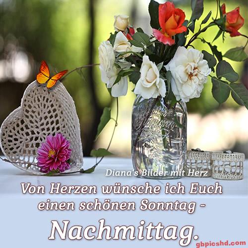 Häkelherz und Blumenglas mit Rosen auf weißem Tisch, orangefarbener Schmetterling, sonniger Hintergrund.