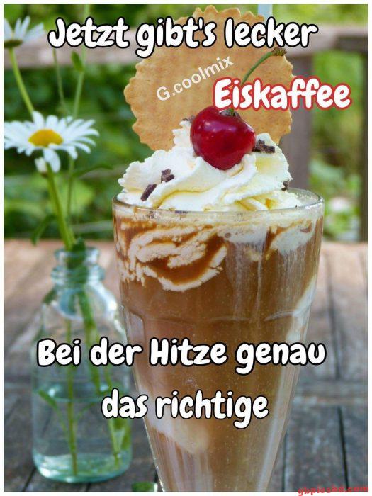 Glas Eiskaffee mit Sahne, Kirsche und Keks auf Holztisch neben Vase mit Gänseblümchen, sommerlich.