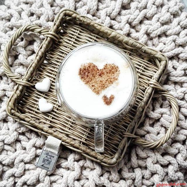 Tasse mit Milchschaum und Zimt-Herzen auf einem Tablett auf grob gestrickter Decke.