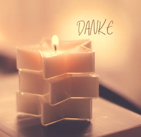 Brennzende Kerze in geformtem Halter, daneben steht das Wort 'Danke'.