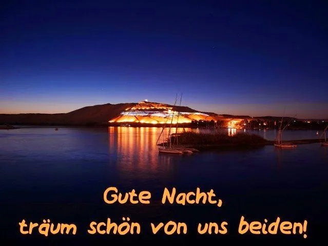 Nachtaufnahme eines beleuchteten Hügels am Wasser mit Booten im Vordergrund.
