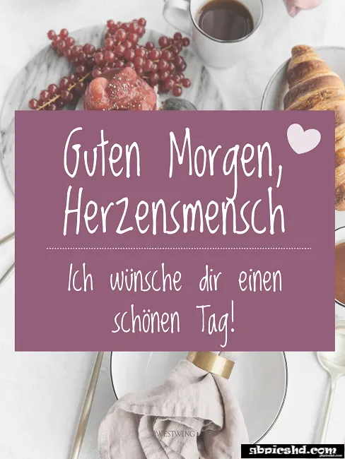 Tasse, Croissant, Brötchen und Trauben auf einem gedeckten Tisch mit Begrüßungstext.